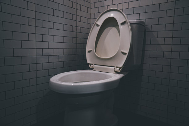 冲水马桶，白色陶瓷马桶近灰墙，侧灯在现代浴室。图片下载