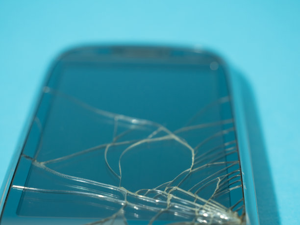 蓝色的桌子上放着黑色的手机，屏幕和机身都破碎了。图片下载