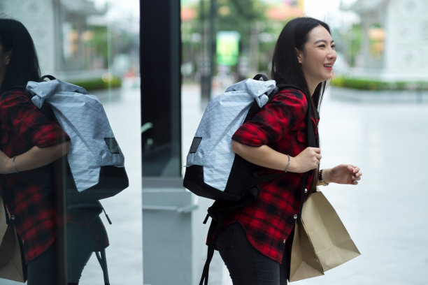 侧面，快乐的年轻女旅行者背着沉重的背包和购物袋图片下载