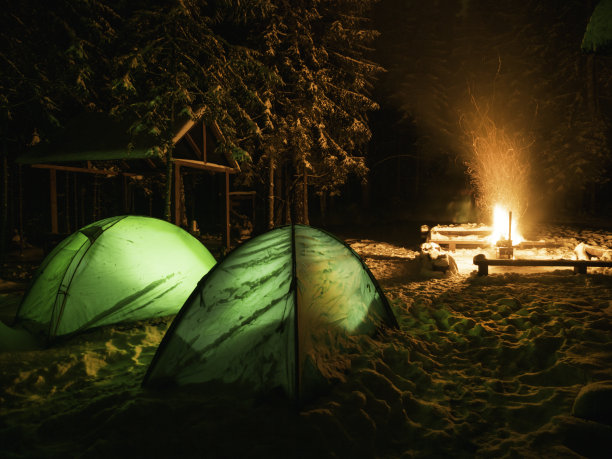 在冬季森林里，围绕营火搭起的两顶绿色帐篷的夜景。在寒冷的季节探索大自然。健康的生活方式。背包全年徒步旅行。图片下载
