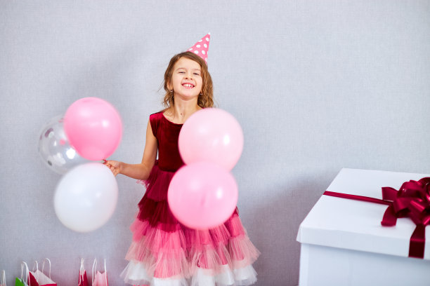可爱，快乐的小女孩在家里的生日派对上，穿着粉红色的裙子和帽子玩气球图片下载