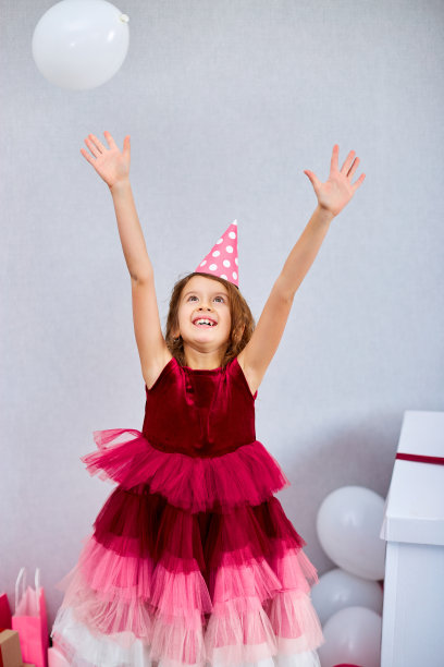 可爱，快乐的小女孩在家里的生日派对上，穿着粉红色的裙子和帽子玩气球图片下载