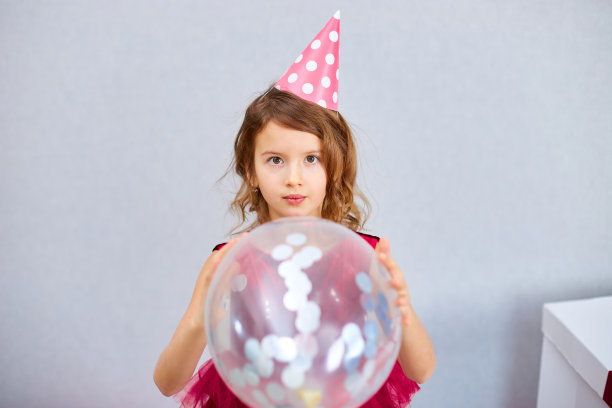 可爱，快乐的小女孩在家里的生日派对上，穿着粉红色的裙子和帽子玩气球图片下载
