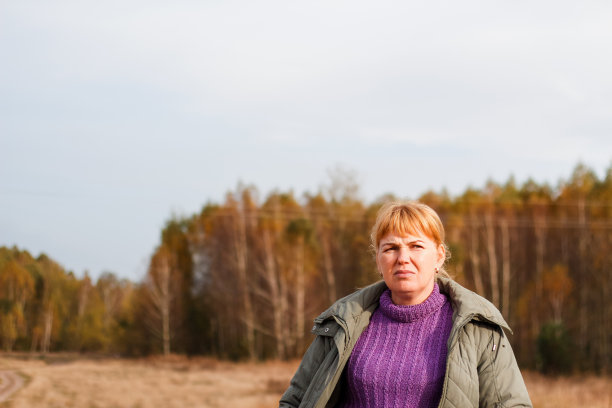 散焦肖像悲伤抑郁的金发40多岁妇女行走在黄色秋天森林自然的背景。穿紫色毛衣的女人。公园,叶子。干燥草地,草地。的焦点图片下载