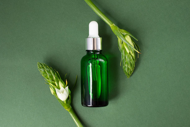 深绿色背景上的绿色化妆品瓶。叶面周围有白花，看上去像镜框。带有复制空间的化妆品模型。图片下载