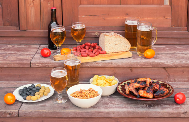 啤酒、啤酒小吃、烤鸡翅、面包和小香肠放在简陋的木梯台阶上。图片下载