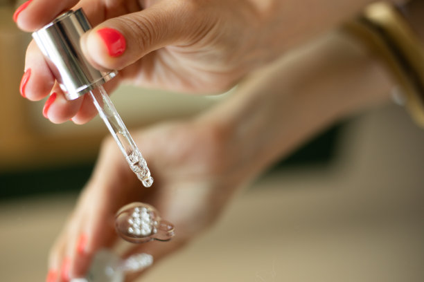 女性手拿滴管。美血清。瓶透明质酸与移液管滴，抗衰老化妆品在美容师手中的金色背景图片下载