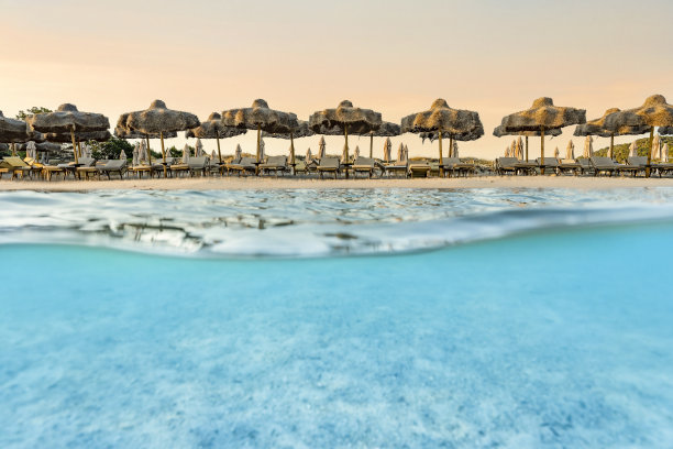 (选择性对焦)分割拍摄，在图片下面。清澈碧绿的海水和一些沙滩伞在令人惊叹的日出中被照亮。意大利撒丁岛的大佩维罗海滩。图片下载