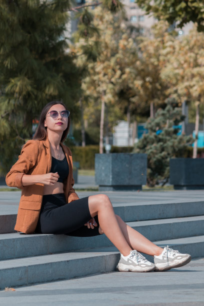 在一个温暖阳光的日子里，戴着太阳镜的女孩坐在公园的台阶上。随机的照片。图片下载