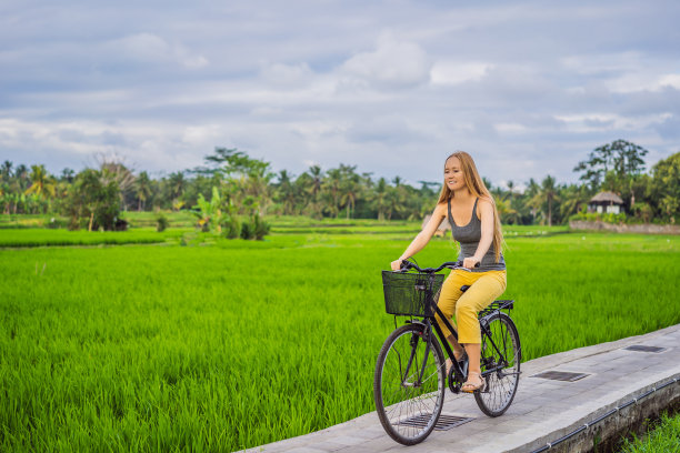 一名年轻女子在巴厘岛乌布的稻田上骑自行车。巴厘岛旅游的概念图片下载