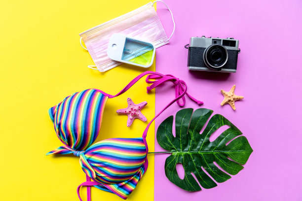 旅行者配件医用口罩，手凝胶洗手液保护新冠病毒与比基尼，粉黄色背景。图片下载