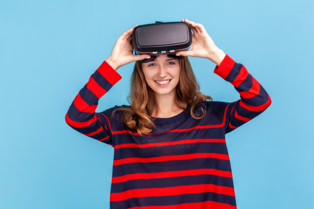 卷发女子身穿条纹休闲风格毛衣，体验虚拟现实耳机，3d仿真，高科技，快乐的表情。图片下载