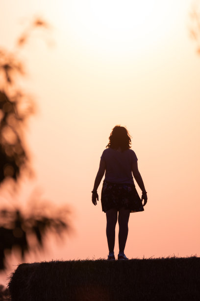 日落时分，一个女人站在草捆上的剪影，太阳在她身后，树枝在她的身体两侧图片下载