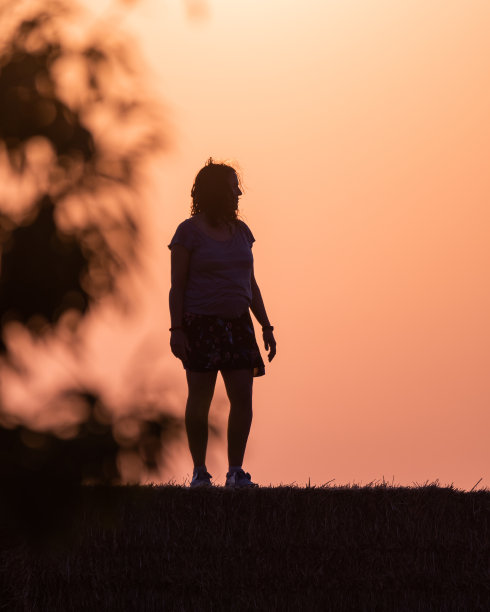 日落时分，一个女人站在草捆上的剪影，太阳在她身后，树枝在她的身体两侧图片下载