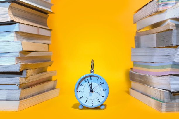 蓝色的闹钟和橙色背景下的一堆书图片下载