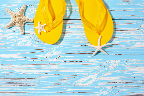 黄色橡胶沙滩人字拖和海星在蓝色木制背景下，放置文字图片下载