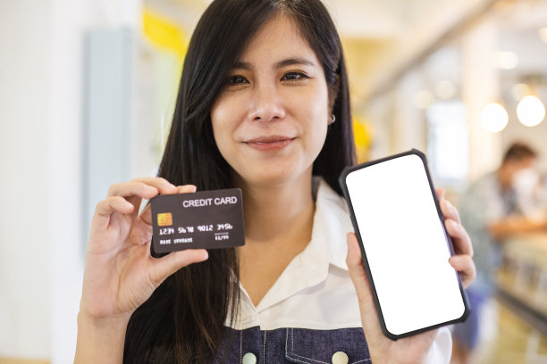 幸福的女人微笑着拿着智能手机，空白的屏幕和信用卡。网上购物和支付的概念。图片下载