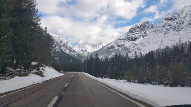 在一个阳光明媚的秋日清晨，一辆电动汽车的驾驶窗向外移动，前面是白雪覆盖的阿尔卑斯山脉。柏油山路上的第一人称视角图片下载