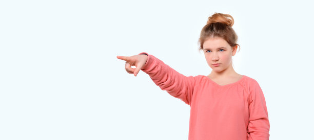 穿着粉色休闲运动衫的年轻女孩惊讶地指着复印室。站在白色的工作室背景下图片下载