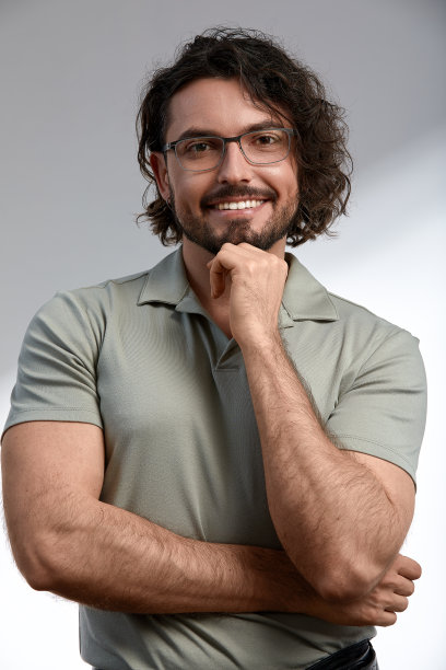 英俊，微笑，年轻男子深色长发和时尚的眼镜孤立在灰色背景，穿着时尚的衣服，积极和成功的事业和业务图片下载