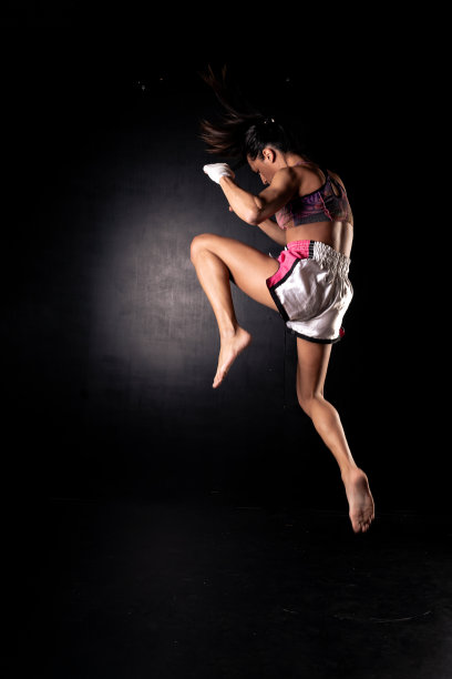 美丽的女子练习武术或踢拳，在踢前在一个位置跳跃。孤立在黑色背景上。图片下载