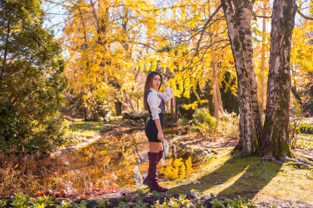 秋天的生活方式，一个年轻的白人黑发，穿着黑色裙子和栗色靴子，看起来很诱人，在湖边的一个公园里图片下载