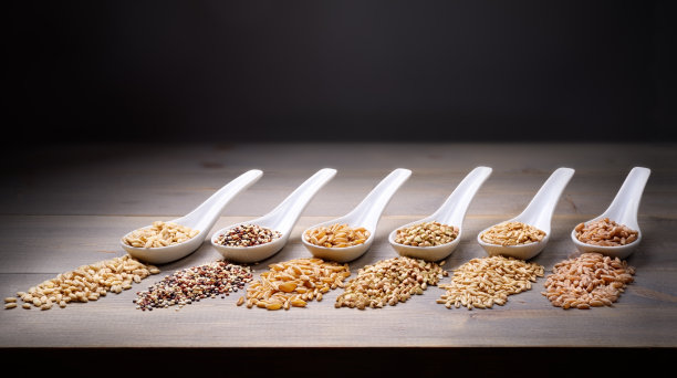 谷物。从左起:大麦、藜麦、小麦呼罗珊、荞麦、燕麦和在木桌上的陶瓷勺子上拼写的文字空间。图片下载