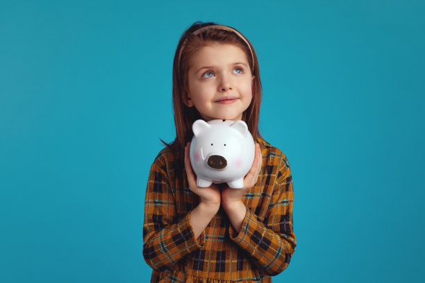 可爱的小女孩抱着储蓄罐，猪的形状靠近脸向上看图片下载