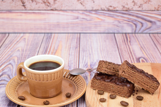 一杯热的黑咖啡和几片巧克力华夫饼。咖啡豆散落在各处图片下载