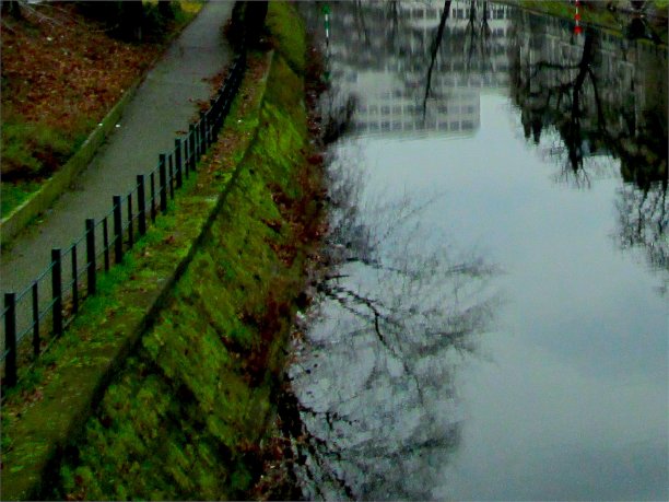 冬天多云的旧城，青苔河岸小路和裸露的树木剪影倒影图片下载