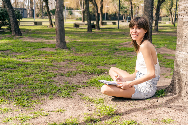 一个微笑的年轻女子在公共广场的小森林里画画。图片下载