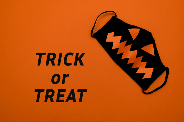 黑色保护面具，橙色背景上有橙色的眼睛和嘴巴。在橙色的背景上玩字母游戏。万圣节和covid-19概念图片下载