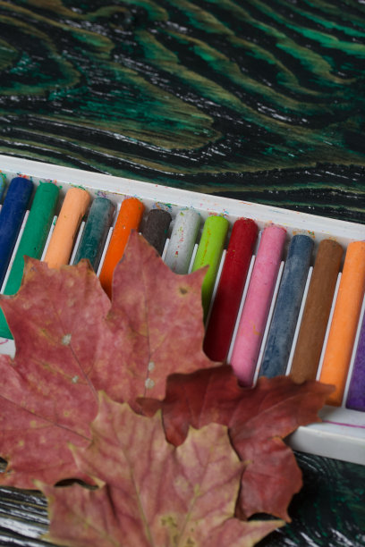 学校用的一套彩色蜡笔。他们躺在松木板上的盒子里。附近秋天的枫叶。图片下载