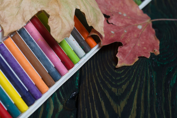 学校用的一套彩色蜡笔。他们躺在松木板上的盒子里。附近秋天的枫叶。图片下载