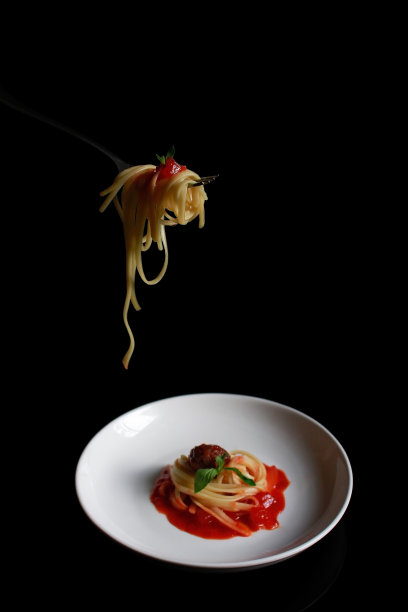 黑色极简风格的白色盘子上挂着一叉意大利面，上面装满了意大利面、肉丸子和番茄酱图片下载