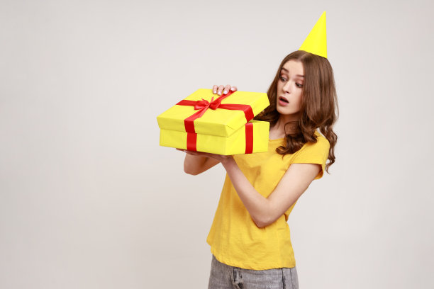 照片中的少女，穿着黄色t恤，打开礼盒，带着惊讶的表情看着里面。图片下载