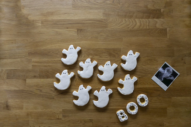 万圣节趴在桌子的底部，桌上放着甜饼干和鬼魂的照片，还有“BOO”的留言。复制空间可以用来填充你想要的内容。图片下载