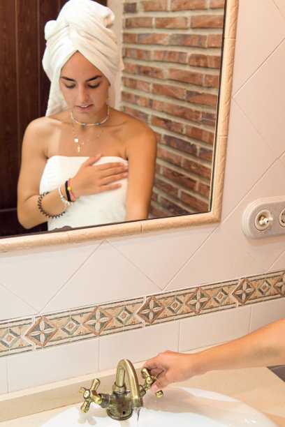 年轻女孩盖着毛巾打开浴室的水龙头映在镜子里。图片下载