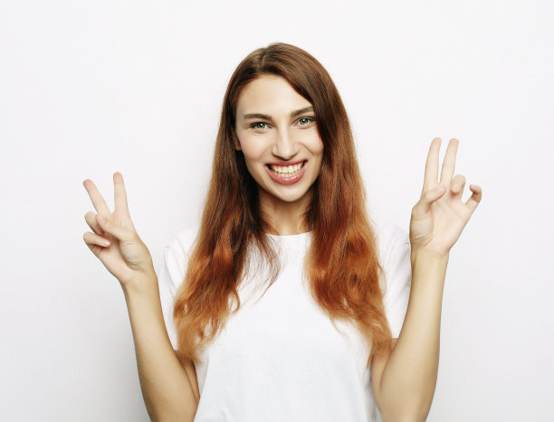 美丽的女人的肖像看着相机微笑和显示和平的手势与手指图片下载