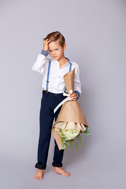 可爱的小男孩手里拿着一束花，背景是灰色的图片下载