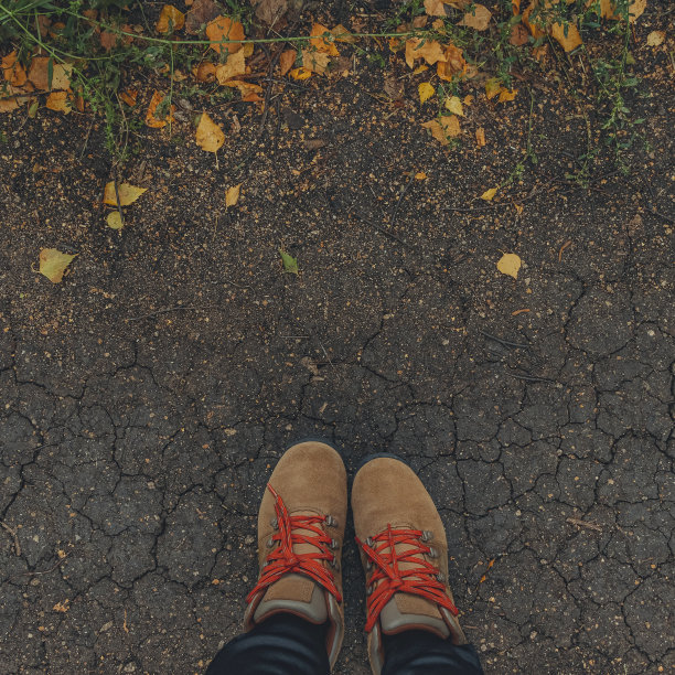 广场形象的脚在棕色的靴子在开裂的地面与黄色的落叶。秋天的背景。生活方式的概念图片下载