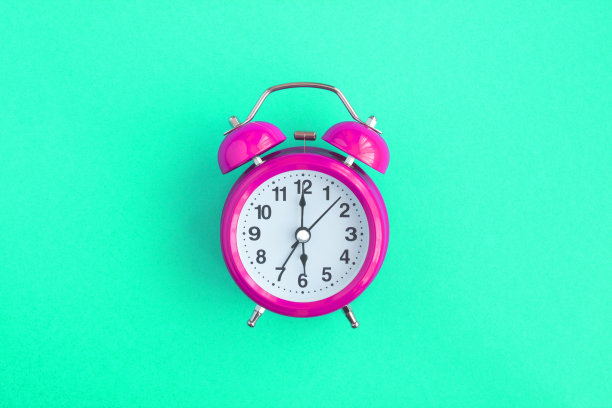 粉色闹钟在绿色背景的中心。特写镜头。副本的空间。图片下载
