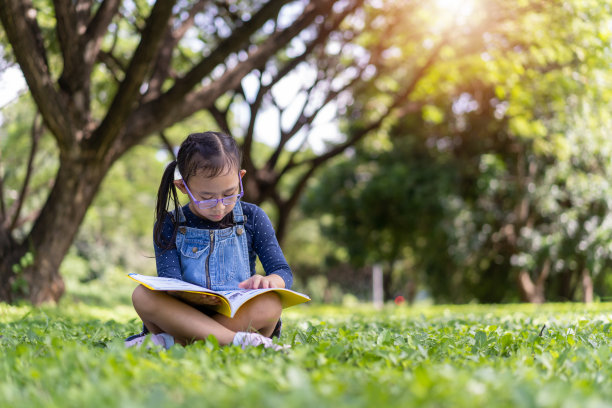快乐的亚洲小女孩在花园里看书图片下载