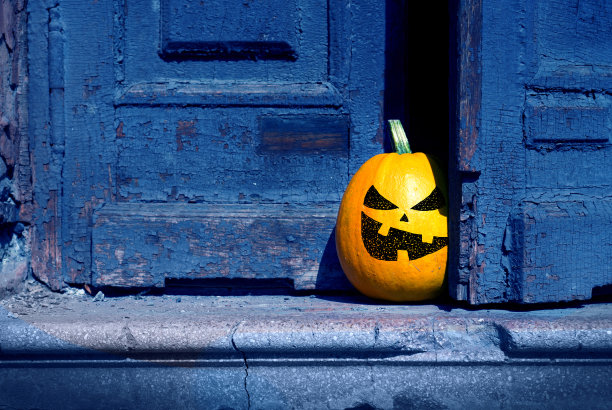 万圣节的背景。一个淘气的南瓜从一扇废弃的旧门后面探出头来。图片下载