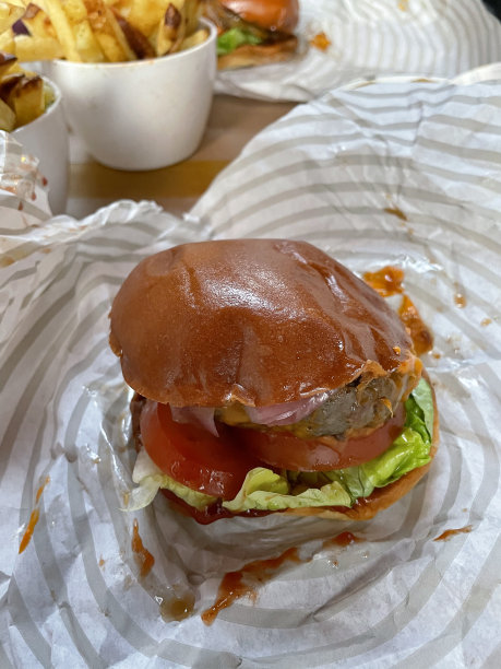 餐厅场景的特写图片，餐桌上有防油纸上的汉堡，快餐牛肉汉堡肉饼在面包，生菜，西红柿和白色的薯片碗，高架视野，聚焦前景图片下载