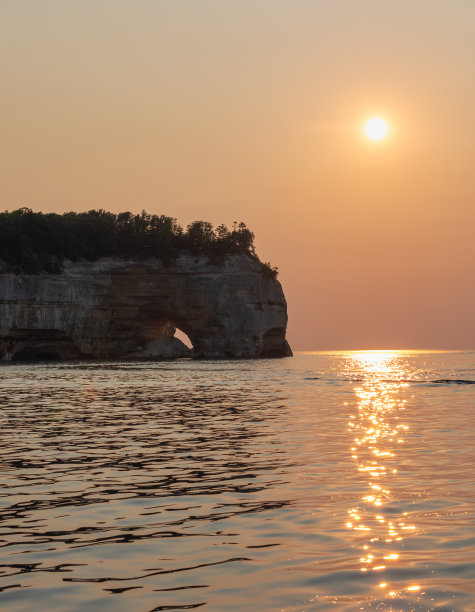 日落通过朦胧的天空上方的一个天然海拱在图片岩石国家湖岸图片下载