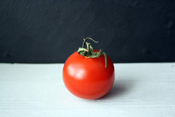 木制背景上有一个红色的西红柿和绿色的小枝。图片下载