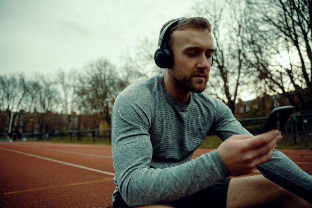白人男性运动员戴着耳机坐在赛道上，手里拿着手机图片下载