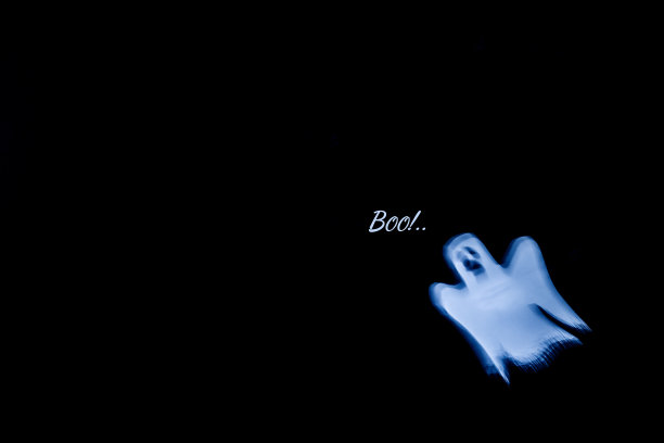 散焦万圣节背景。黑色背景上的一个模糊的白色幽灵。铭文嘘!复制文本空间。图片下载