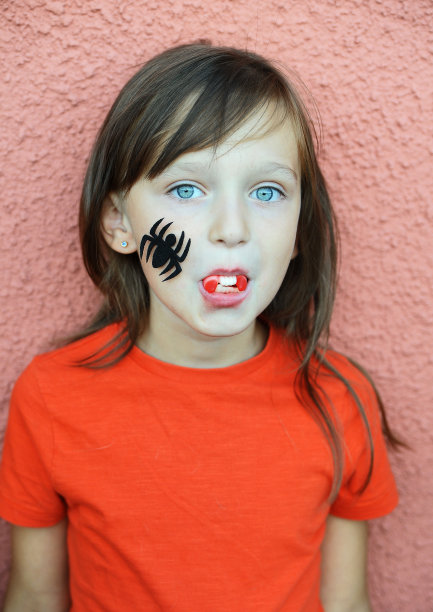 万圣节主题：红背景下脸上有蜘蛛的橙色T恤女孩图片下载